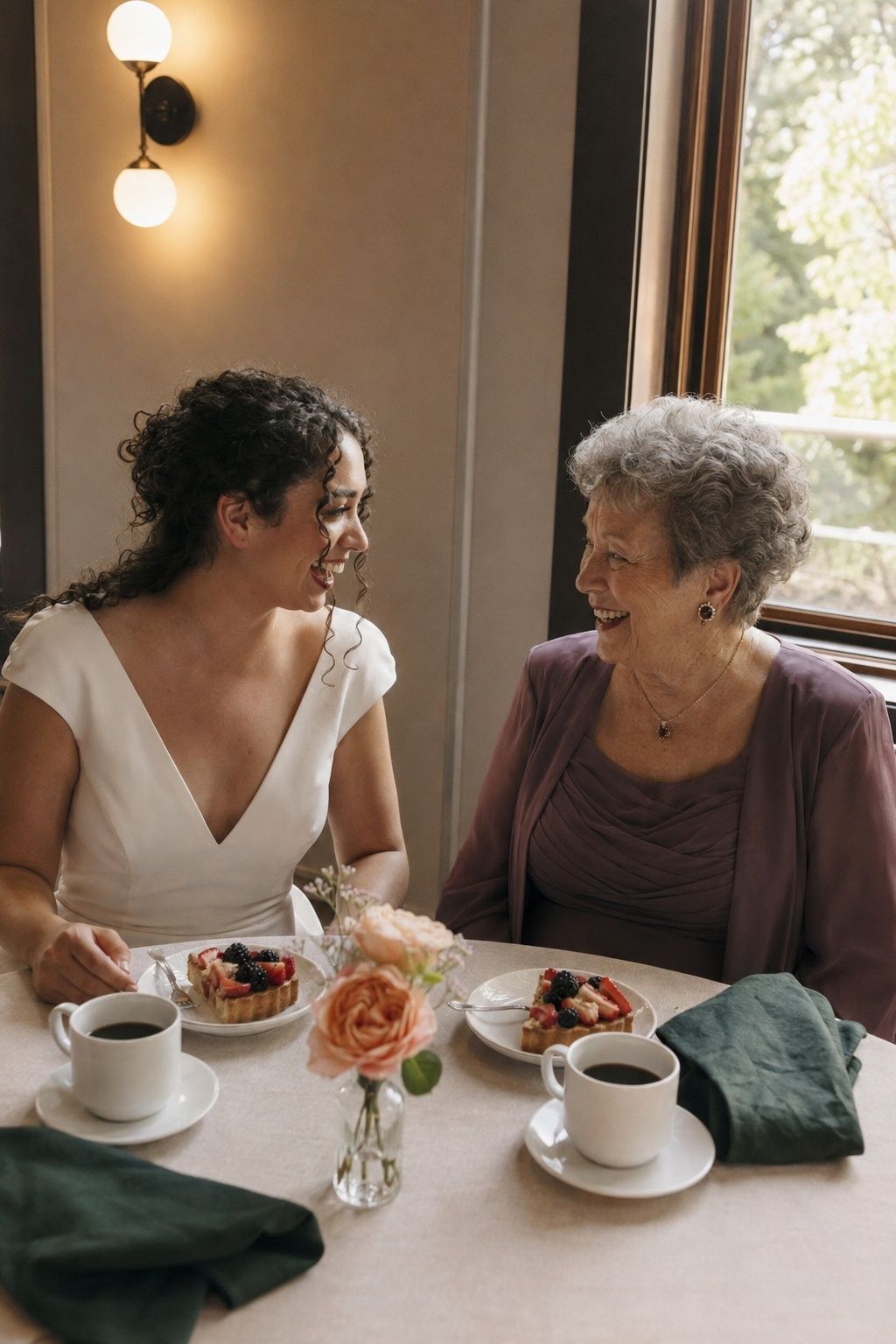 Bride and grandmother laughing together over dessert and coffee.