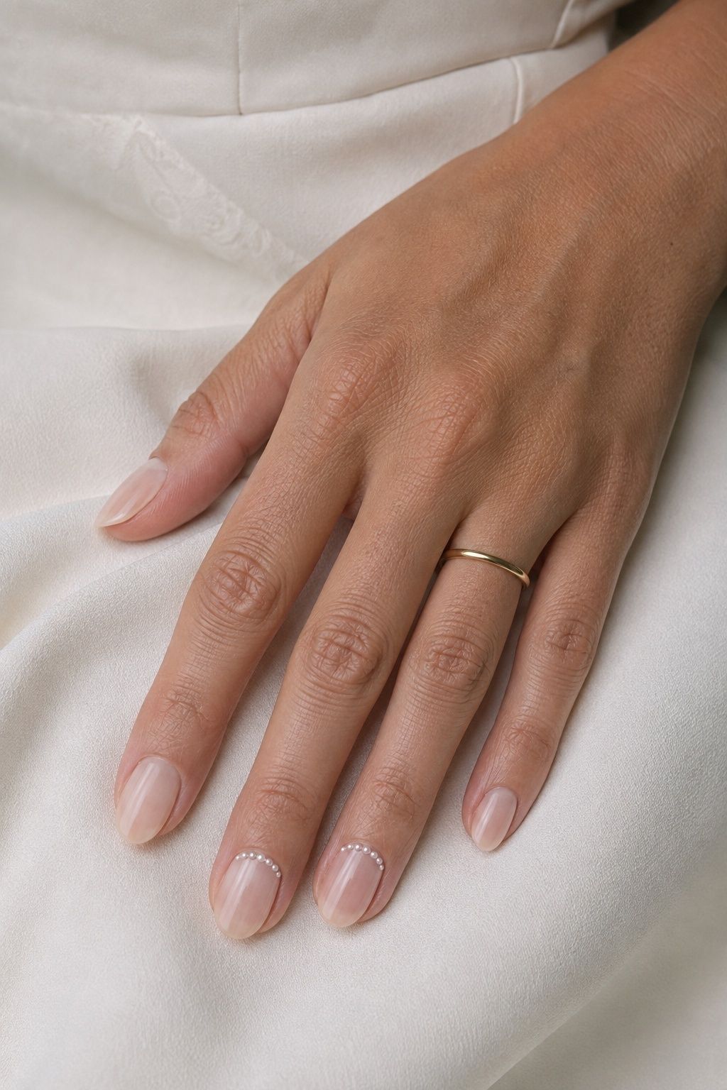 Tiny pearl dots along two nail cuticles on a sheer nude bridal manicure
